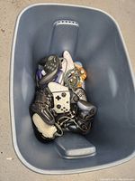 Thirteen assorted video game controllers in a blue plastic bin, showing varied styles and colors, all tangled together.