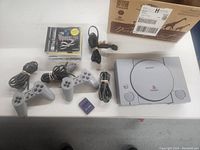 Full lot overview showing the Sony PlayStation 1 console, two wired controllers, a memory card, power and AV cables, and four game discs including Resident Evil 2.