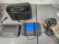Two Element portable DVD players shown beside power cords, composite AV cables, and a black soft carrying case with compartments.