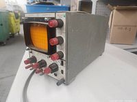 Front and side view of Telequipment D51 oscilloscope showing orange CRT screen, control knobs, and ports with power on and indicator light illuminated.