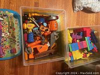 Clear bin with assorted plastic toy tools including drills, saws, screwdrivers in orange, blue, yellow colors.