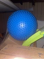 Photo of a large blue inflatable exercise ball covered with evenly spaced small spikes, placed on top of some cardboard boxes and next to a green plastic item.