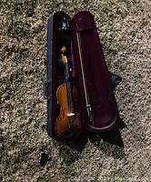 Children's violin placed inside an open black hard case with burgundy velvet lining, along with a violin bow.