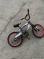 Photo showing a blue kids bike with pink rims laid on pavement. The bike has visible wear and is missing grips on handlebars, appears to need repair.