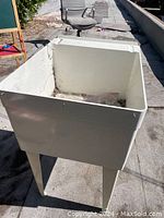 Photo of a large white mop sink with legs outdoors on pavement in sunlight.
