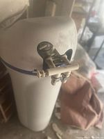 Photo of a white GE water softener, model GXSF30H, showing the top portion with a manual valve handle and plumbing fittings, set indoors with surrounding items out of focus.