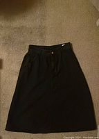 Black skirt laid flat showing front side with button and pockets