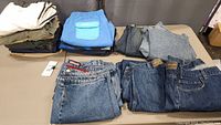 Photo showing men's shorts folded in stacks and five pairs of denim jeans laid out on table.