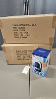 Factory sealed boxes containing 12 pieces each of Zaahn Ultra Chill personal cooler and humidifier. One box open with single unit boxed in front.