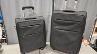 Overview photo of two black Bentley suitcases, smaller (22") and larger (26"), side by side showing front zippered compartments and wheels.