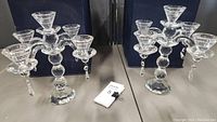 Pair of clear crystal candelabras displayed on table, each with three candleholders and hanging crystal prisms, with storage boxes behind them.