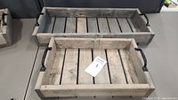 Two rustic wooden trays stacked with large one behind smaller. Both have metal handles and wooden slat bases.