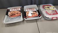Front view of three 13x9 inch baking pans, two without lids and one with a plastic lid, all new with cookbooks attached.
