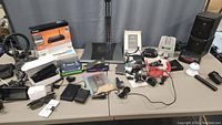 Photo showing whole electronics lot with routers in boxes, speakers, label printer, chargers, cables and miscellaneous electronic devices on table