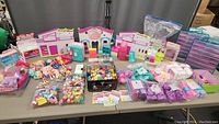 Photo showing wide variety of Shopkins collectibles, dolls, and play set components spread across table.