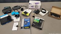 Lot overview showing multiple electronics including chargers, remote controls, smart watch, and boxed items