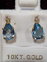 Close-up front view of the earrings showing pear-shaped blue topaz stones and round moissanite stones above them, mounted on 10K gold settings.
