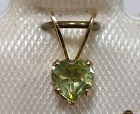 Close-up frontal view of heart-shaped peridot gemstone set in 14K yellow gold.