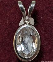 Front view of the oval faceted aquamarine gemstone set in 14K white gold pendant on a maroon fabric background.