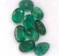 Close-up top view of ten green oval and pear-shaped emerald cabochon gemstones on white background