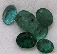 Close-up photo of six loose emerald cabochon gemstones showing color and inclusions.