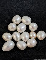 Close-up of 15 fresh water pearls on black background showing oval and rounded shapes and natural luster.