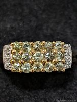 Close-up front view of the ring showing green sapphire stones with white topaz accents on a sterling silver band