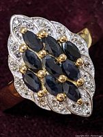 Close-up image of sterling silver ring with a cluster of marquise sapphires in the center, surrounded by white topaz stones with gold-tone prong settings.