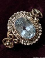 Close-up image of sterling silver ring with oval faceted blue topaz gemstone and decorative beaded silver bezel and band detail.