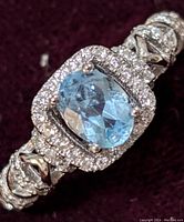 Close-up front view of the sterling silver ring showing oval blue topaz center stone and double halo of clear cubic zirconia stones.