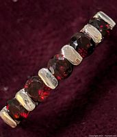 Close-up image showing dark red garnet stones faceted and arranged in line with sterling silver links, on a dark fabric background.