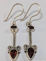 Close-up front view of pair of sterling silver dangle earrings with garnet stones showing design details and stones.