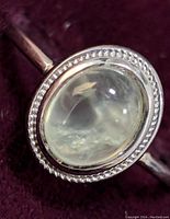 Close-up of the oval clear cabochon gemstone set in silver with detailed silver border around the stone and smooth band visible.
