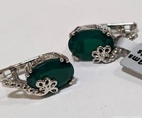 Close-up photo showing the front side of the pair of earrings with green onyx stones held by silver prongs and floral decorations.