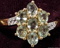 Close-up image of ring top showing 7 oval green sapphire stones in cluster with gold-tone prongs and surrounding silver band details.