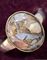 Close-up of oval-shaped Muhave turquoise cabochon stone with golden veining set in sterling silver ring. Ring band and stone visible from multiple angles on a dark background.