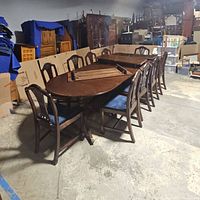 Wide view of the antique wooden dining table with 10 blue upholstered mahogany chairs and 3 leaves placed on table.