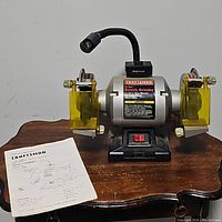 Front view of Craftsman 6-inch bench grinder on a wooden table with included instruction manual.