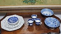 View showing two different sized blue and white porcelain bowls, three blue floral tea cups, four matching saucers, and a stack of blue floral plates.