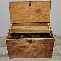 Closed large wood chest for tool storage showing wood grain, latch on the front, and internal tray visible over open lid.
