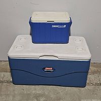 Photo showing both coolers stacked: smaller blue Coleman PolyLite 28 on top of large blue Coleman Xtreme 5 with white lid and cup holders