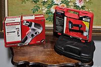 Photo showing boxed Craftsman Hammerhead 12 volt auto-hammer and Craftsman Air Drive Brad Nailer in case on table.