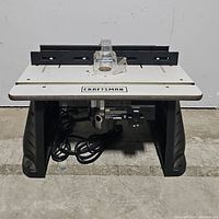 Front view of the Craftsman router table showing the work surface, adjustable fence, and safety guard with power cord underneath.