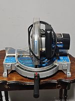 Front-facing view of the Delta 10" compound power miter saw showing the base, blade guard, and handle with power cord wrapped around.