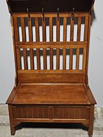 Front view of brown wooden hall tree with slatted back, 4 coat hooks, and storage bench seat.