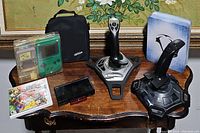 Photo shows gaming joysticks, Nintendo green Game Boy handheld, Mario Kart Nintendo DS game, additional game cartridge, and black carrying bag
