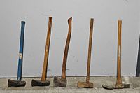 Five hand tools against a white wall; includes four wooden-handled axes and one blue-handled axe.