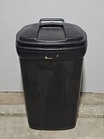 Front view of large black plastic wheeled trash can with hinged lid and handle.