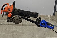 Side view of Black+Decker 3-in-1 leaf blower with collection bag attached and Kobalt 26-inch hedge trimmer lying on the ground.