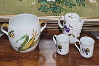 Photo of gold-handled porcelain jar featuring corn decoration and two coffee cups with grape designs